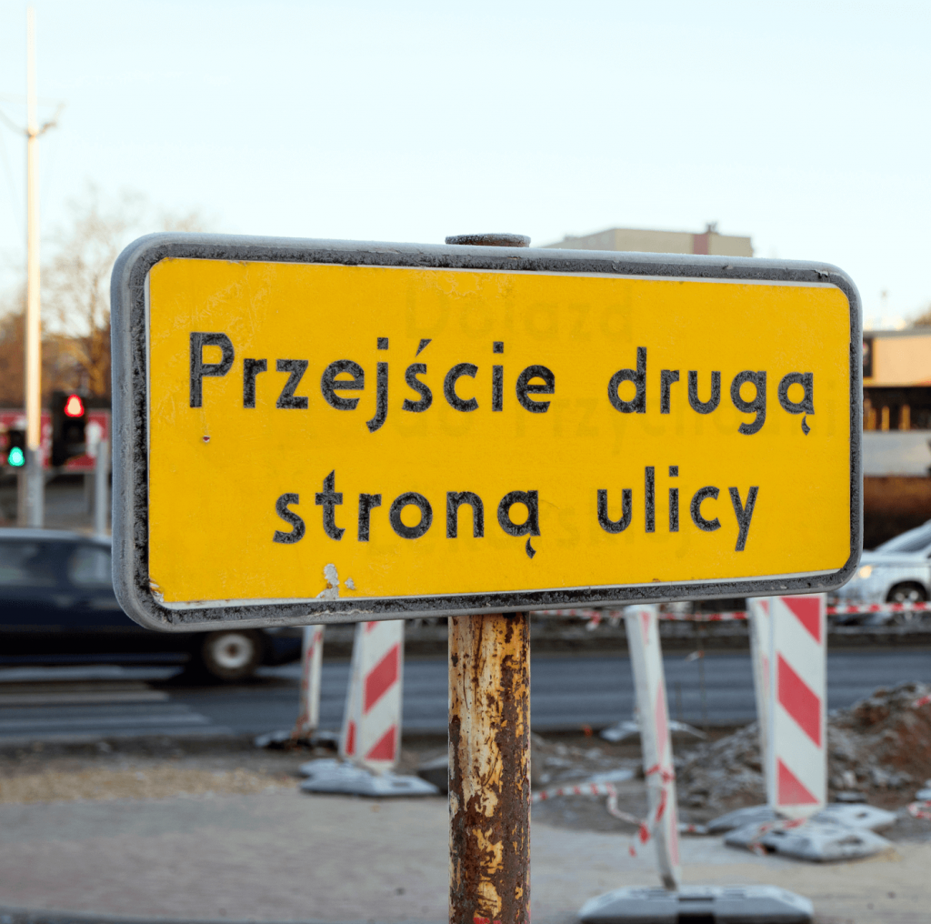 Znak uzupełniający dla pieszych, informujący o przejściu drugą stroną ulicy 